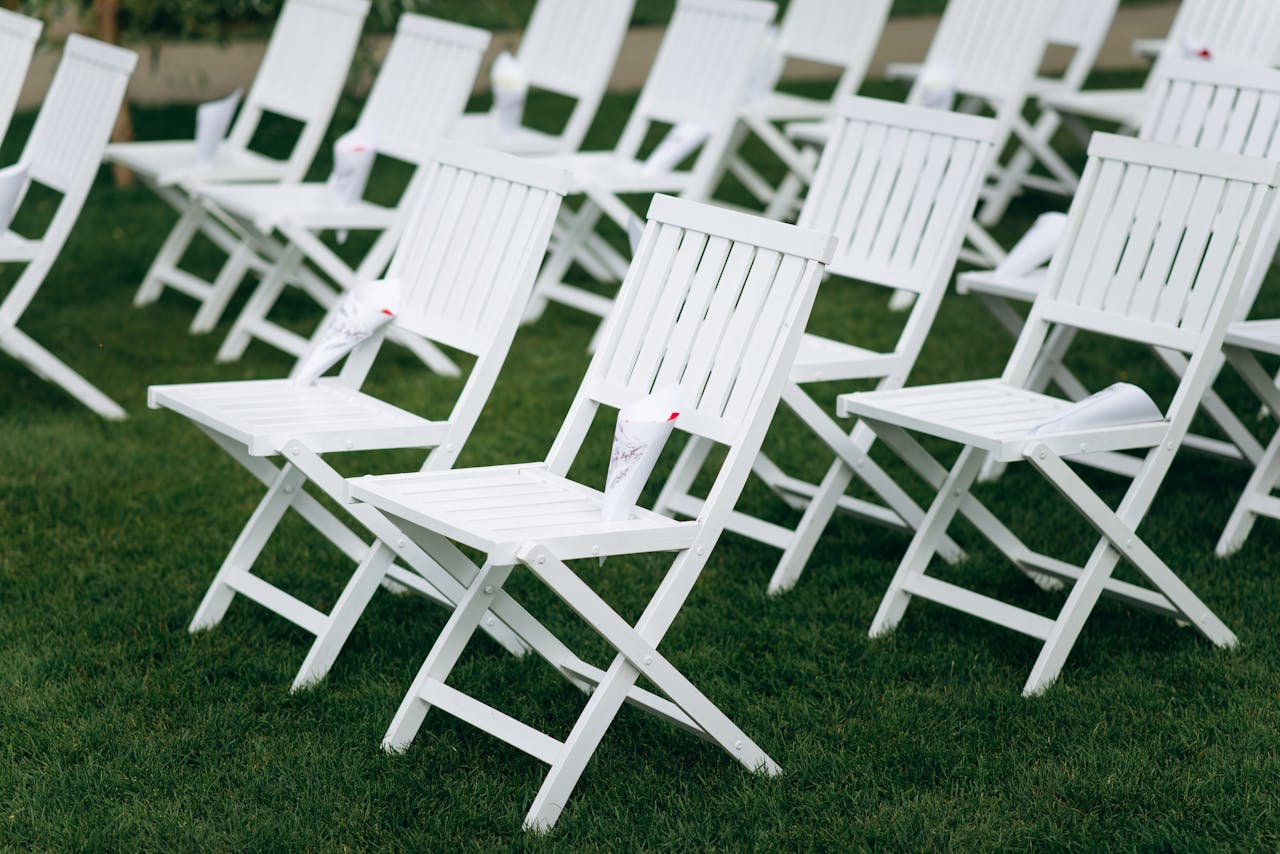 Rows of white folding chairs arranged neatly on a grassy field for an outdoor event.