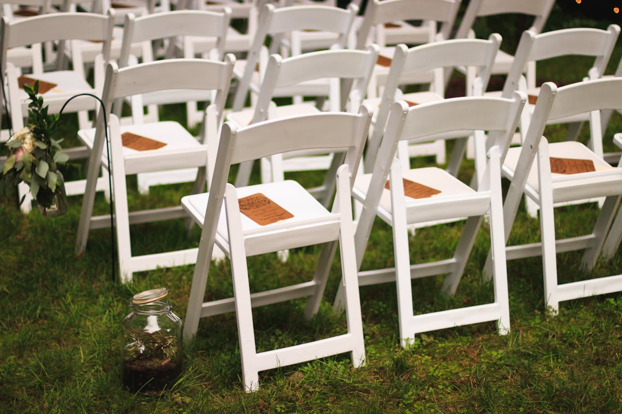White wooden chairs arranged in a garden setting, perfect for an outdoor wedding or event.