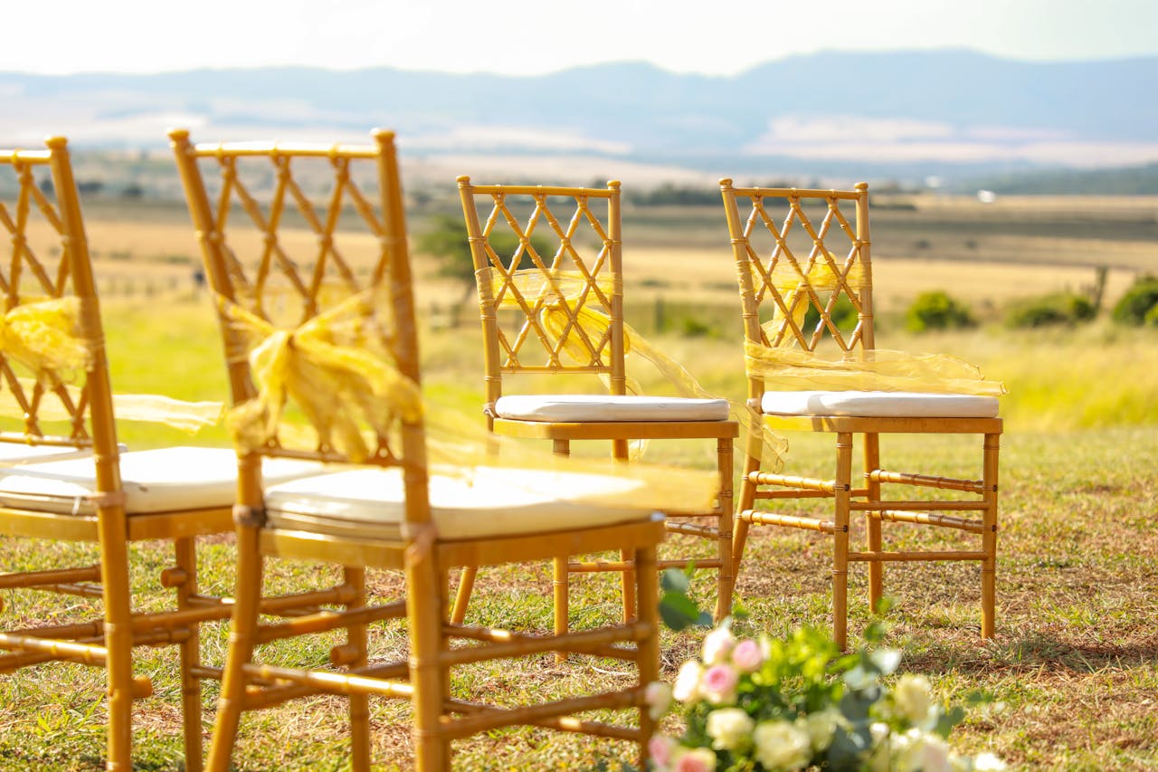 Elegant outdoor wedding ceremony setup with wooden chairs in a sunny field.
