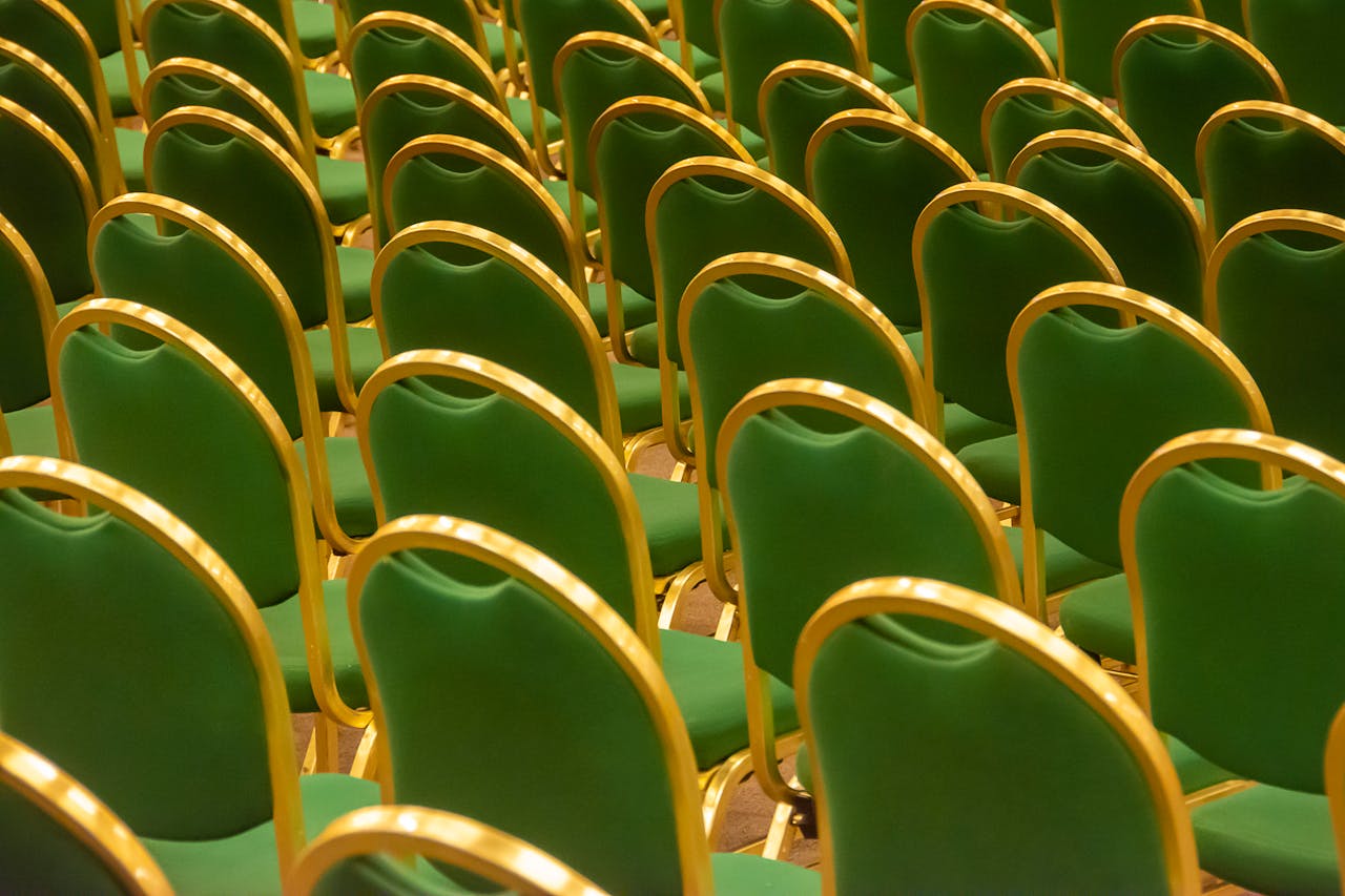 Symmetrical arrangement of green chairs in an empty auditorium, ready for an event.