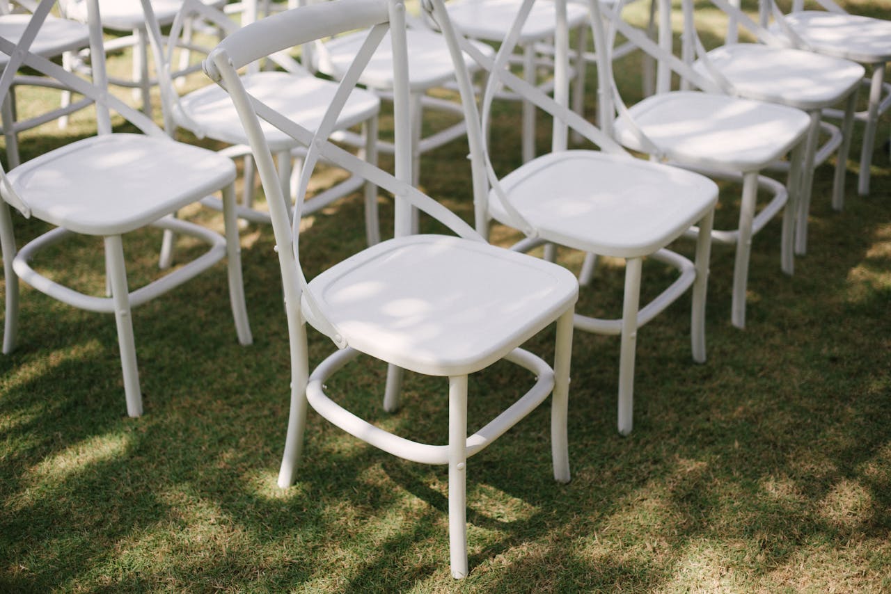 Rows of elegant white chairs arranged outdoors for a wedding ceremony on a sunny day.