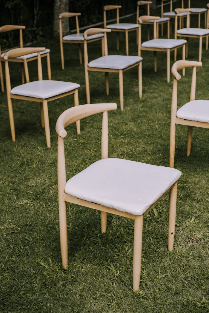Wooden chairs arranged on green grass at an outdoor event setting, perfect for weddings or gatherings.