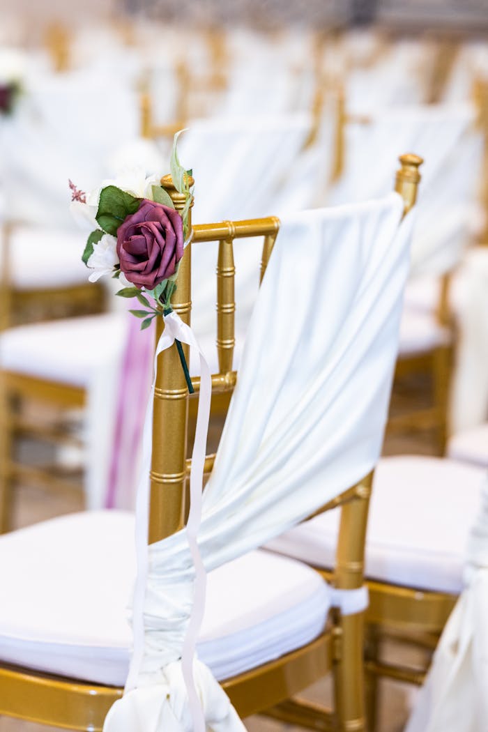 A beautifully decorated wedding chair with white drape and floral arrangement, capturing elegance and romance.