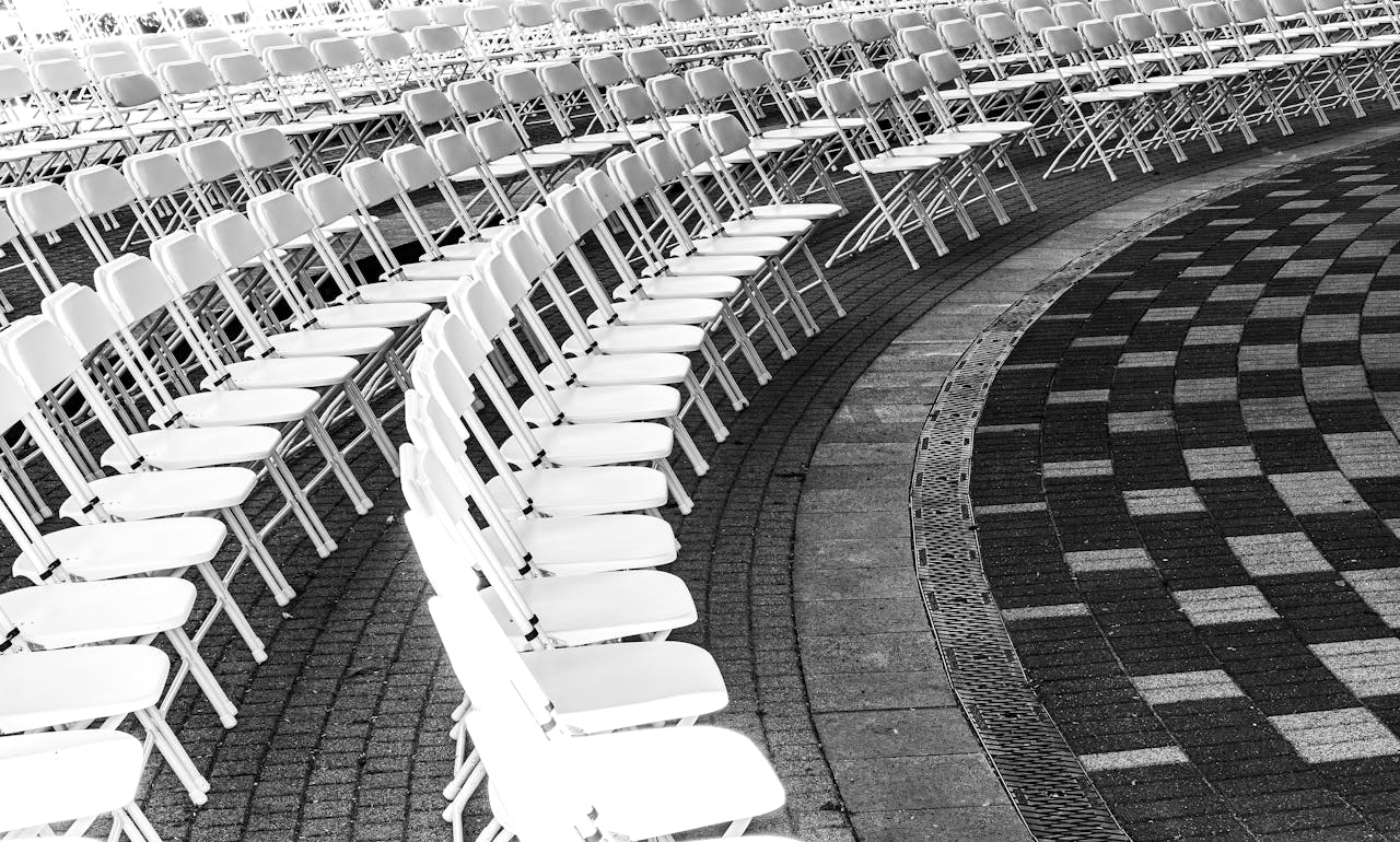 Black and white image of white chairs arranged in curved rows on a checkered outdoor pavement.